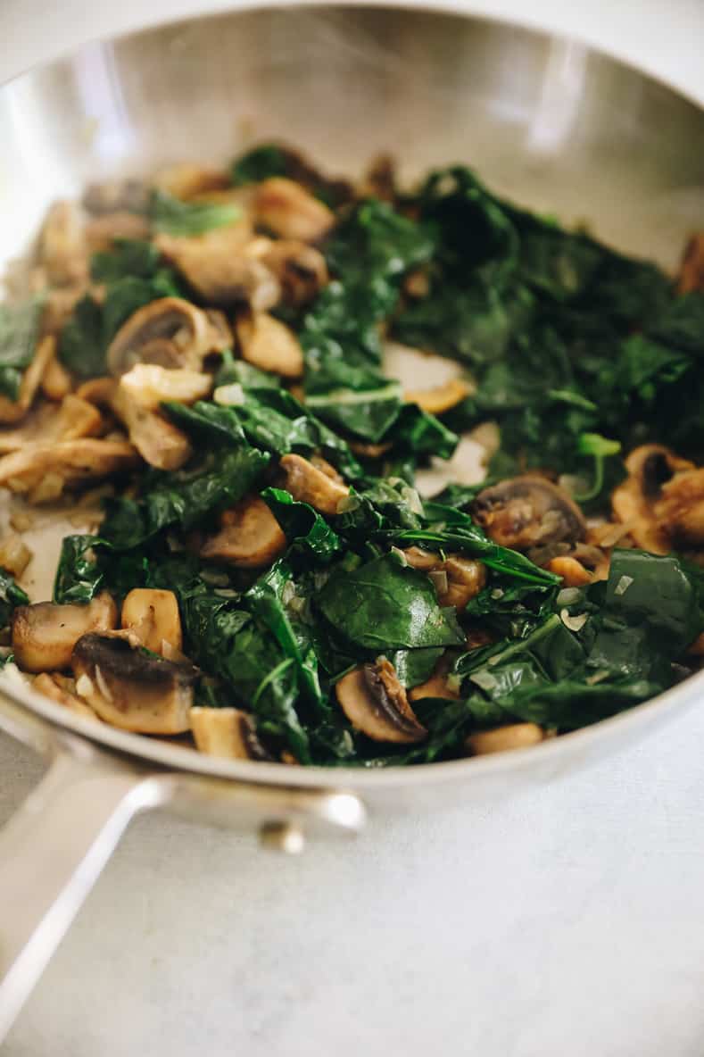 A sautรฉ pan with mushrooms and greens.